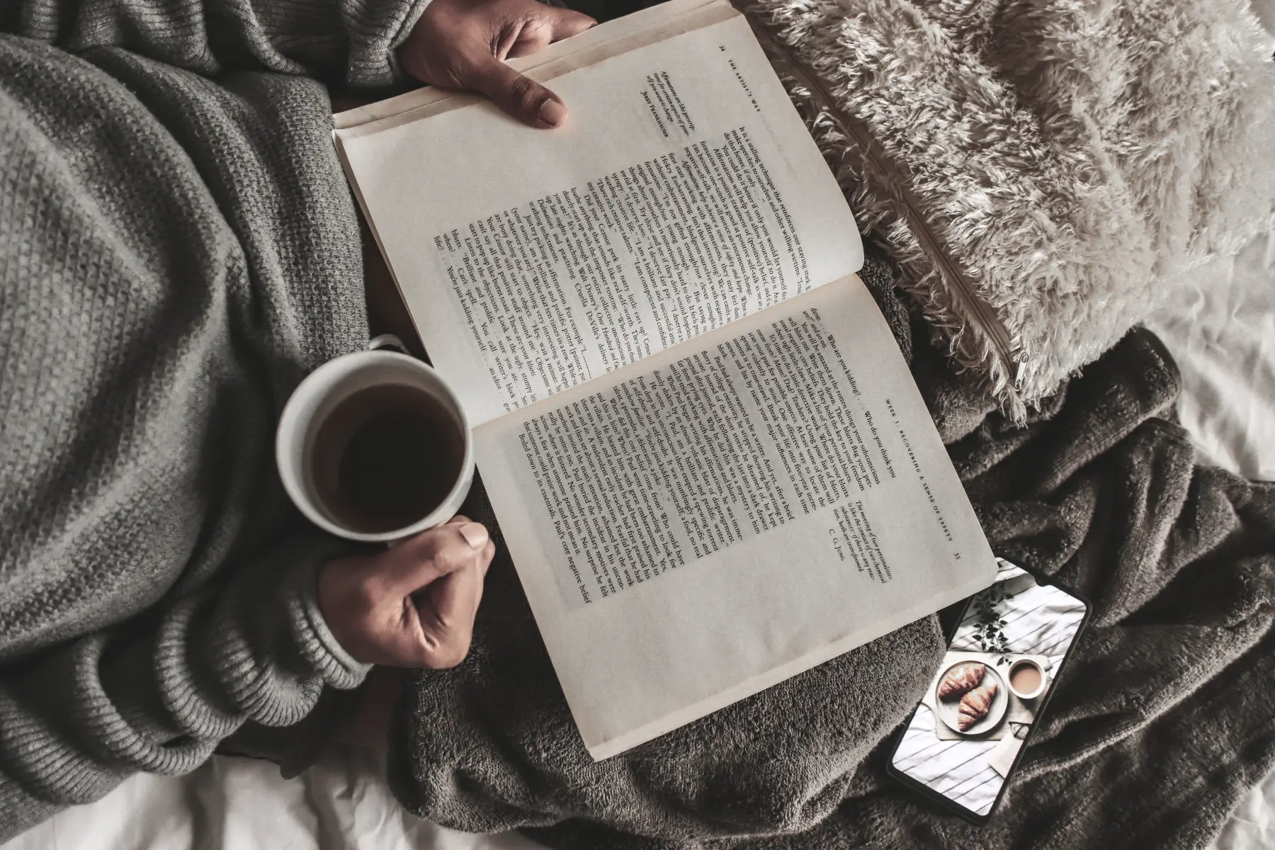 An open book and a cup of coffee on a soft blanket