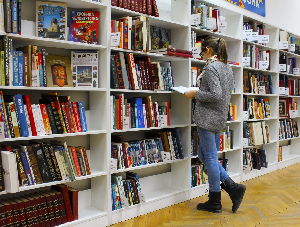 A reader browsing books on white bookstore shelves